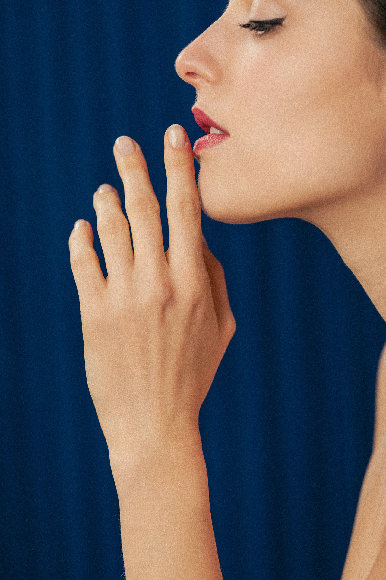 Photographie d'une jeune femme de profil amenant sa main devant sa bouche