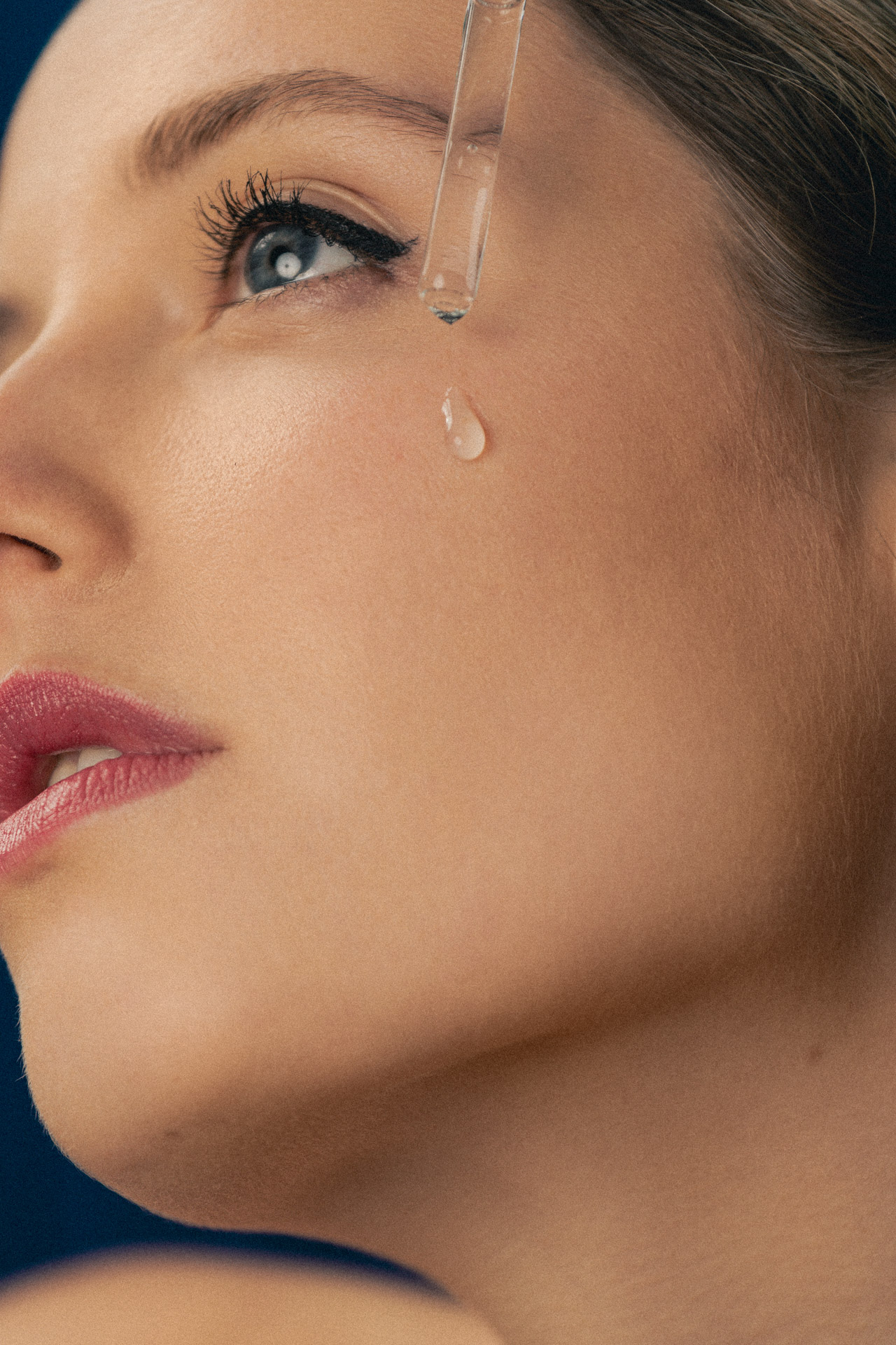 Photographie d'une goutte de sérum hydratant ruisselant sur la joue d'une jeune femme